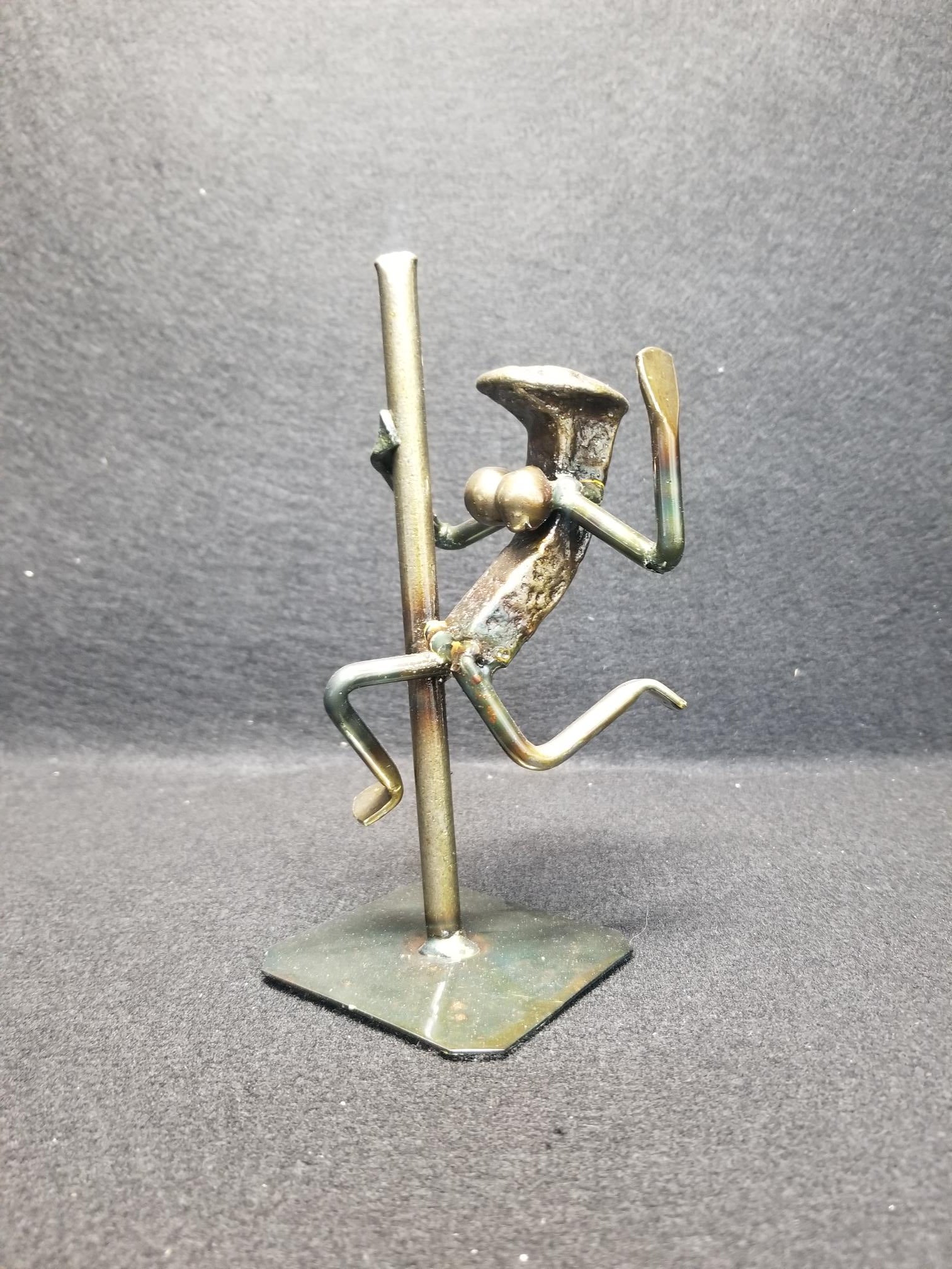Exotic Dancer swinging with one hand on the pole metal spike art. This item is approx. 7 inches tall. Variations are common.
