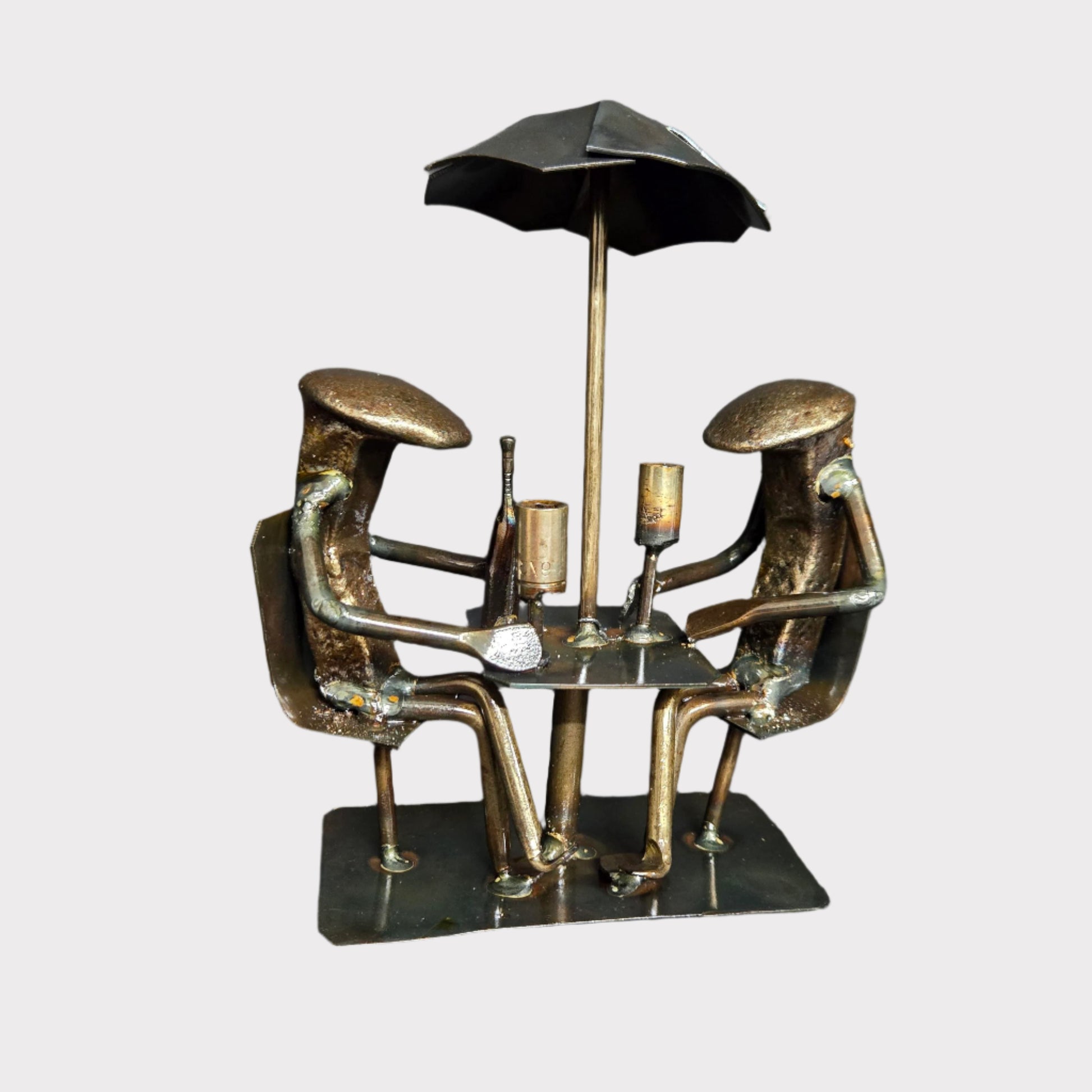 Two figures are seated under an umbrella, talking over wine. Each piece is handmade and unique; minor details may vary.